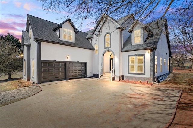 view of front of property featuring a garage, driveway, a shingled roof, and stucco siding