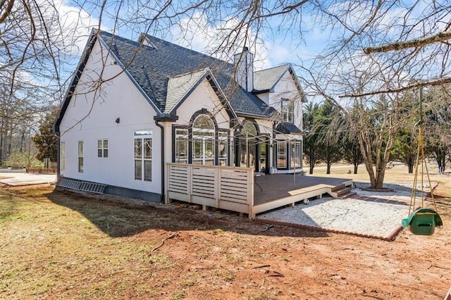 rear view of house featuring stucco siding, roof with shingles, a chimney, and a wooden deck