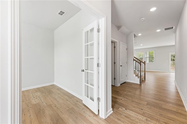 hallway with stairs, baseboards, visible vents, and light wood-style floors