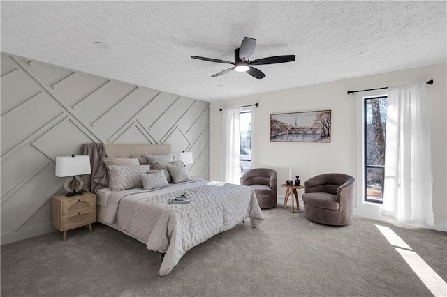 carpeted bedroom with multiple windows, ceiling fan, a textured ceiling, a decorative wall, and baseboards