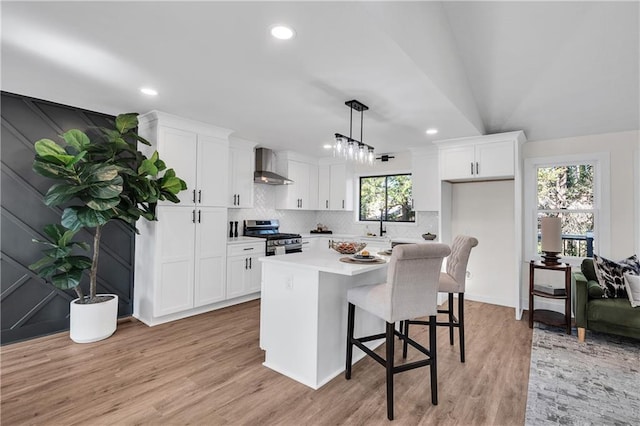 kitchen with gas range, white cabinetry, decorative light fixtures, and wall chimney range hood