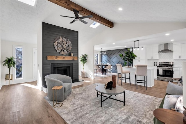 living room with a ceiling fan, light wood finished floors, a large fireplace, recessed lighting, and a skylight