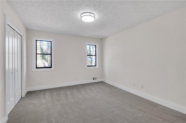 unfurnished bedroom featuring carpet floors, baseboards, a textured ceiling, and a closet