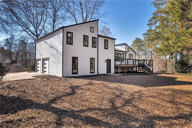 rear view of house with an attached garage, a deck, stairway, and driveway
