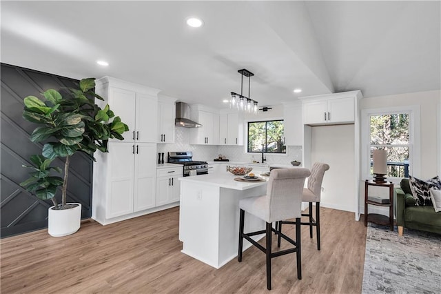 kitchen with wall chimney exhaust hood, stainless steel gas range, white cabinets, tasteful backsplash, and recessed lighting