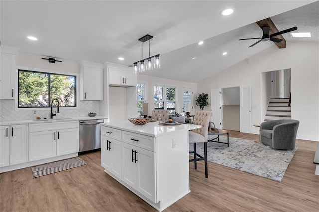 kitchen featuring dishwasher, a sink, a kitchen breakfast bar, tasteful backsplash, and light wood-style floors
