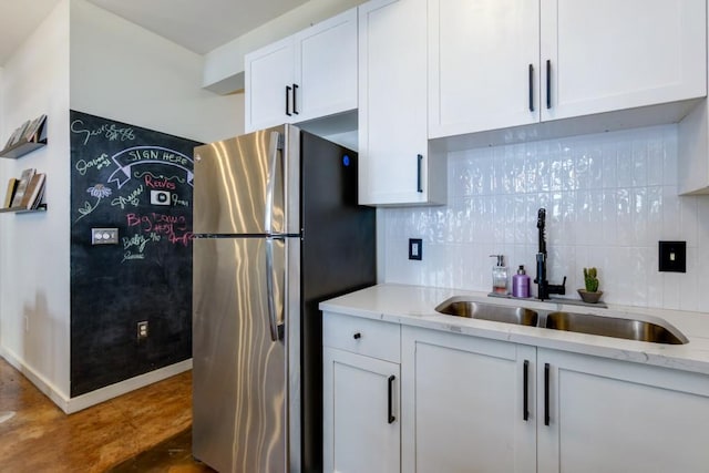 kitchen with backsplash, white cabinets, freestanding refrigerator, and a sink