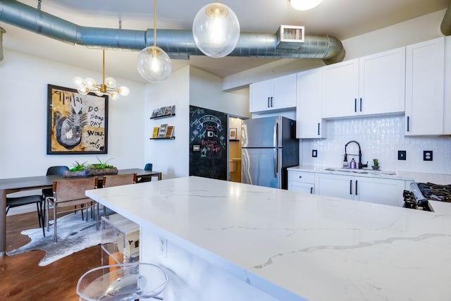 kitchen featuring light stone counters, visible vents, freestanding refrigerator, a sink, and tasteful backsplash