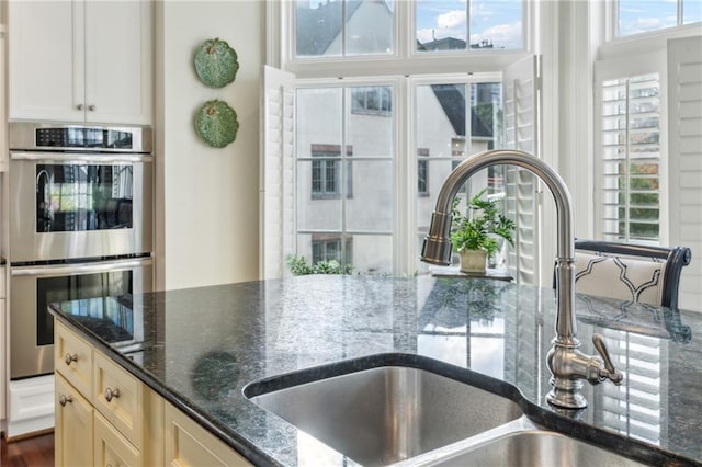 kitchen featuring white cabinets, double oven, dark stone countertops, and sink