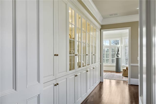 hall with dark wood finished floors, baseboards, ornamental molding, and visible vents