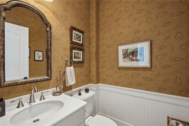 half bath featuring toilet, vanity, and a wainscoted wall