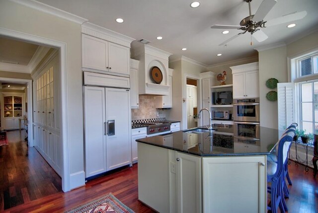 kitchen featuring dark stone counters, a kitchen island with sink, sink, dishwasher, and dark hardwood / wood-style floors