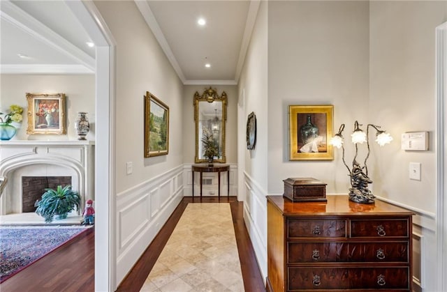 hallway with crown molding, a decorative wall, recessed lighting, wood finished floors, and wainscoting