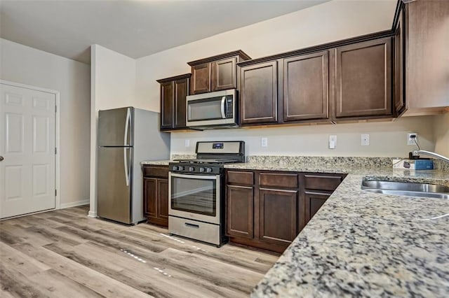 kitchen with dark brown cabinetry, light stone countertops, sink, stainless steel appliances, and light wood-type flooring