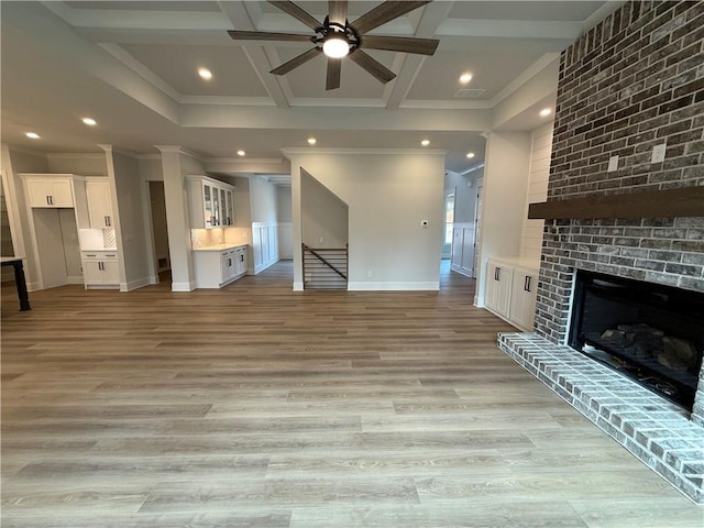 unfurnished living room with ceiling fan, beamed ceiling, crown molding, a fireplace, and light wood-type flooring