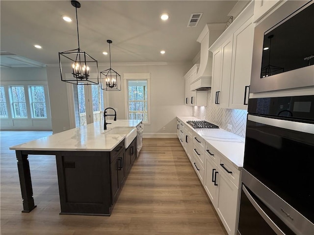 kitchen with ornamental molding, white cabinetry, a healthy amount of sunlight, and an island with sink