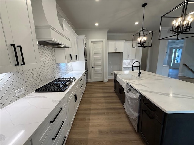 kitchen featuring custom exhaust hood, white cabinets, sink, an island with sink, and decorative light fixtures