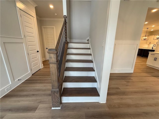 stairs with a chandelier, hardwood / wood-style flooring, and ornamental molding