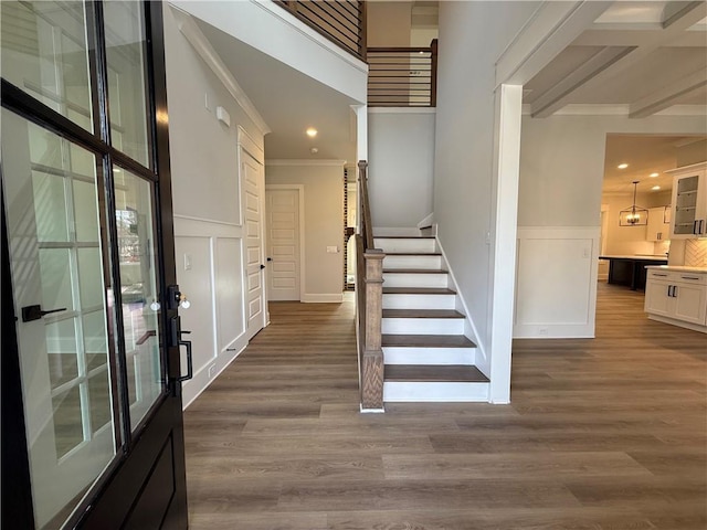 foyer featuring beam ceiling, crown molding, wood-type flooring, and a notable chandelier