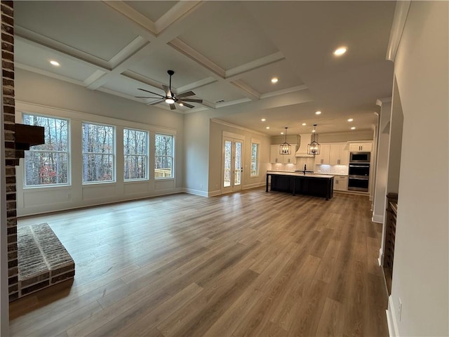 unfurnished living room with beam ceiling, ceiling fan, wood-type flooring, and coffered ceiling