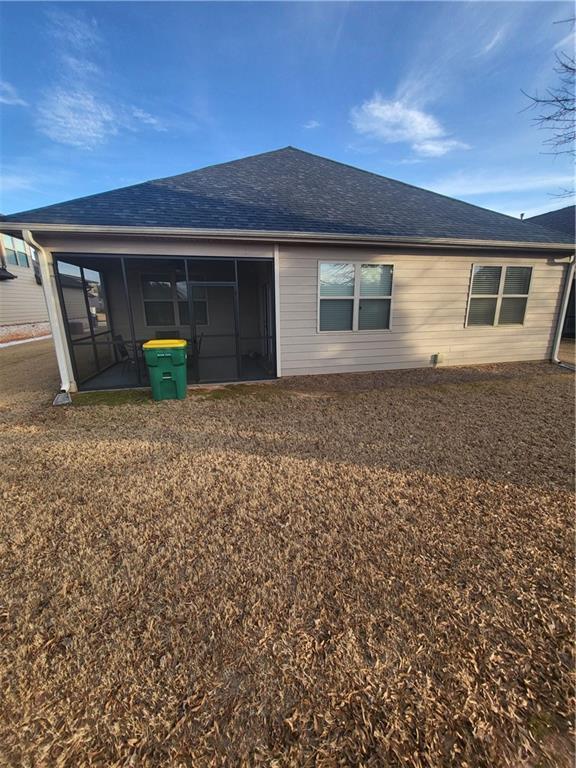 rear view of property featuring a sunroom, roof with shingles, and a yard