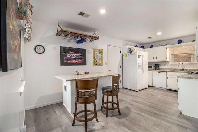 kitchen with sink, white appliances, a breakfast bar area, white cabinetry, and light wood-type flooring