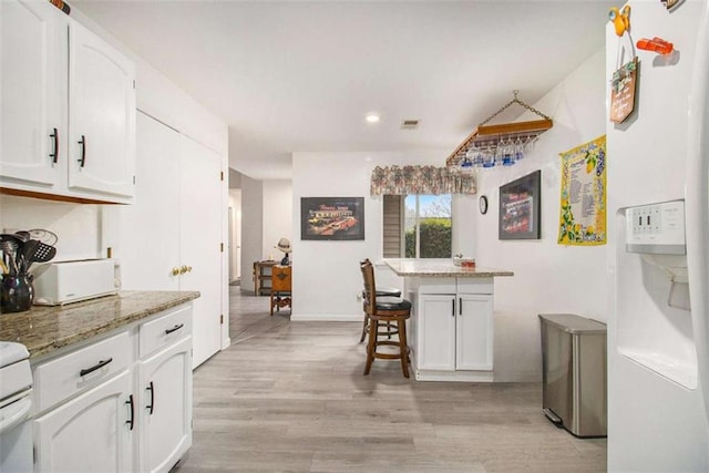 kitchen with white cabinetry, light stone counters, white refrigerator with ice dispenser, a kitchen bar, and light wood-type flooring