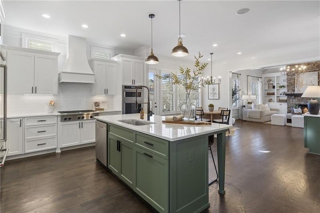 kitchen featuring appliances with stainless steel finishes, a kitchen breakfast bar, custom range hood, green cabinetry, and a center island with sink