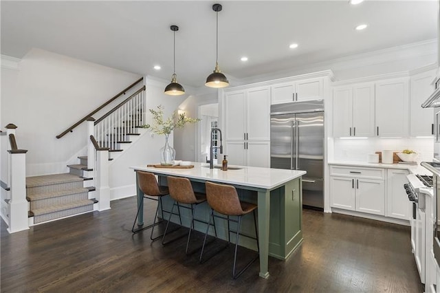 kitchen featuring built in fridge, sink, white cabinets, gas range, and a center island with sink