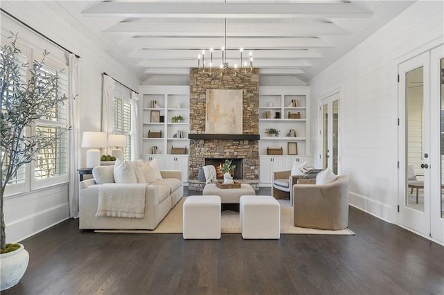 living room featuring dark wood-type flooring, a notable chandelier, lofted ceiling with beams, built in shelves, and a stone fireplace