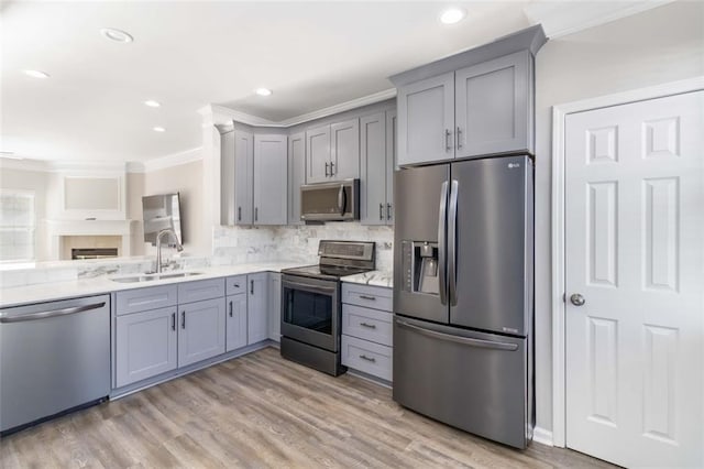 kitchen with ornamental molding, gray cabinets, light wood-style floors, stainless steel appliances, and a sink