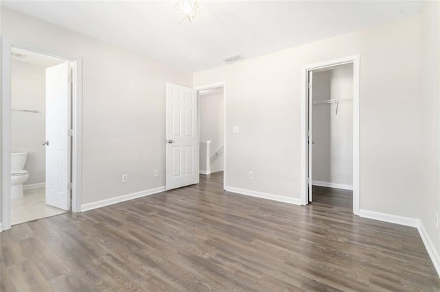 unfurnished bedroom featuring a walk in closet, baseboards, dark wood-style flooring, and a closet