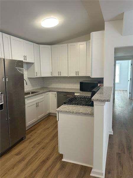 2041 Olive Springs Rd, Marietta, GA 30060 - kitchen featuring a peninsula, a sink, white cabinets, dark wood-type flooring, and decorative backsplash