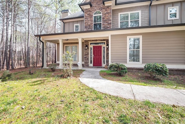 view of front of home featuring stone siding, a porch, board and batten siding, and a front yard