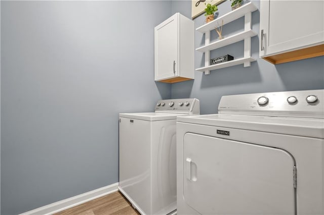 clothes washing area featuring wood finished floors, baseboards, cabinet space, and washer and clothes dryer
