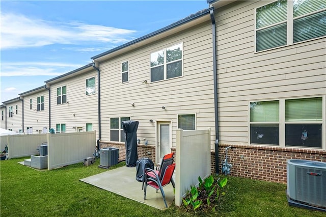 rear view of house featuring a lawn, brick siding, cooling unit, and fence
