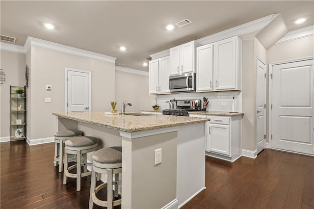 kitchen with crown molding, stainless steel appliances, dark wood finished floors, and a center island with sink
