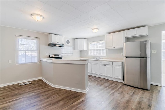 kitchen with under cabinet range hood, wood finished floors, white cabinetry, light countertops, and appliances with stainless steel finishes