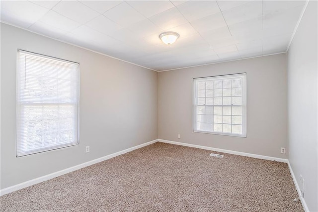 empty room with carpet floors, visible vents, crown molding, and baseboards