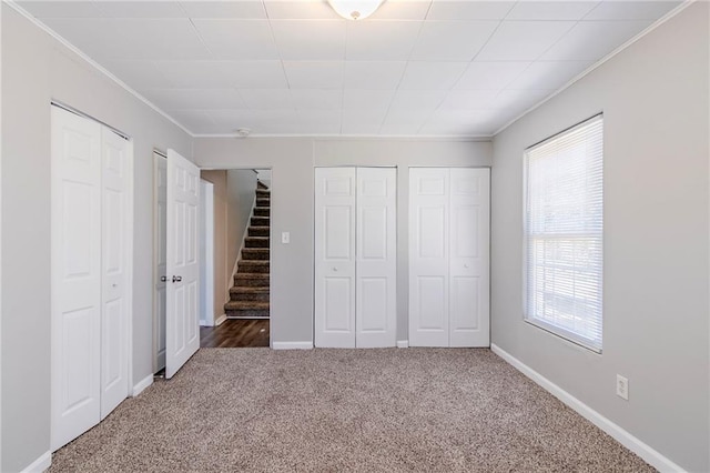 unfurnished bedroom featuring baseboards, carpet, ornamental molding, and two closets