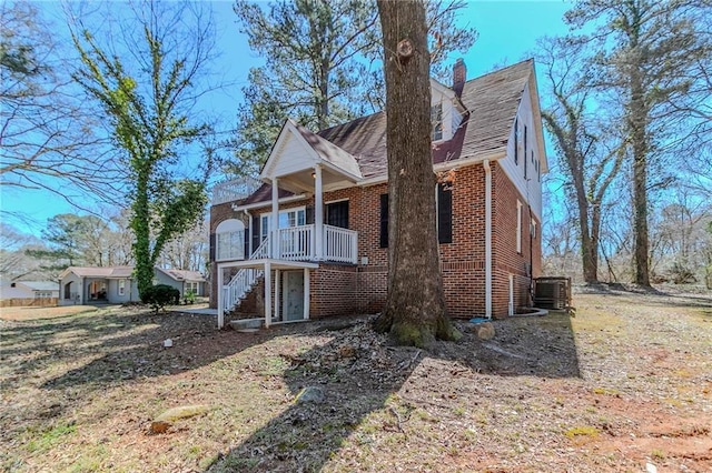 view of front of house featuring stairs, brick siding, a chimney, and central air condition unit