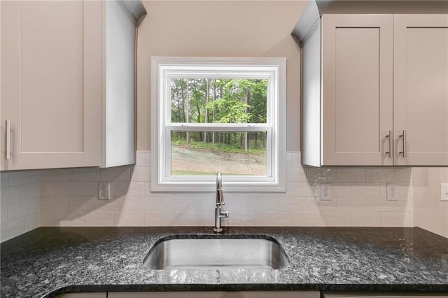 kitchen with sink, white cabinetry, backsplash, and dark stone counters