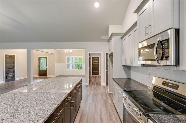 kitchen featuring light wood-type flooring, light stone countertops, tasteful backsplash, stainless steel appliances, and a chandelier