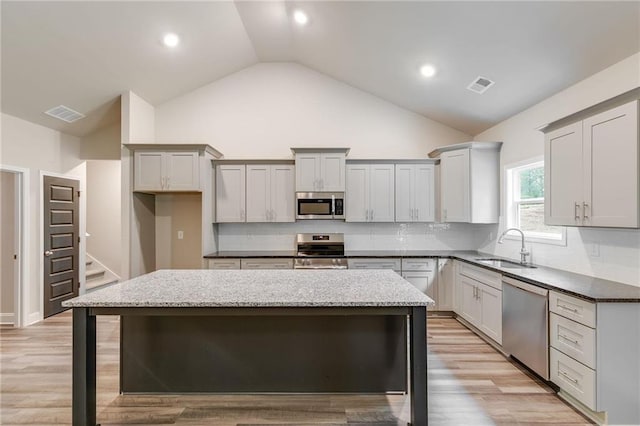 kitchen with sink, a center island, light stone counters, decorative backsplash, and appliances with stainless steel finishes