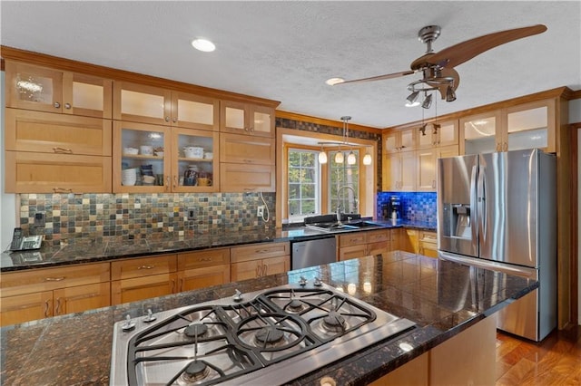 kitchen with sink, hanging light fixtures, dark stone counters, light hardwood / wood-style floors, and appliances with stainless steel finishes