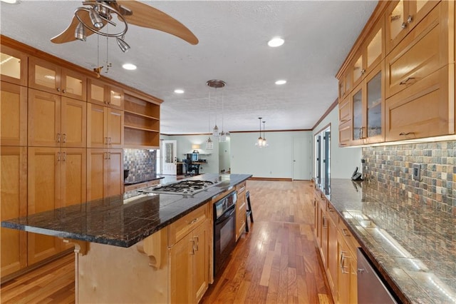 kitchen with a kitchen breakfast bar, tasteful backsplash, light hardwood / wood-style floors, stainless steel gas stovetop, and black oven