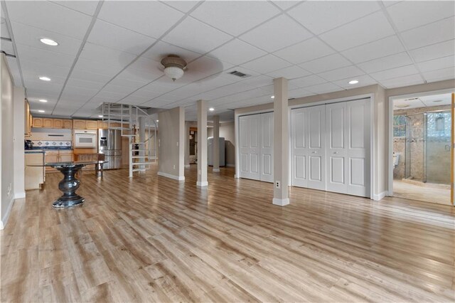 workout area with a paneled ceiling and light wood-type flooring