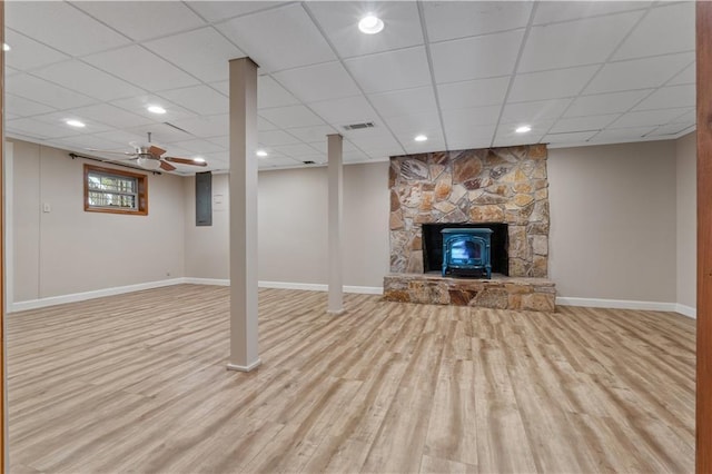 basement featuring a wood stove, a paneled ceiling, and light wood-type flooring