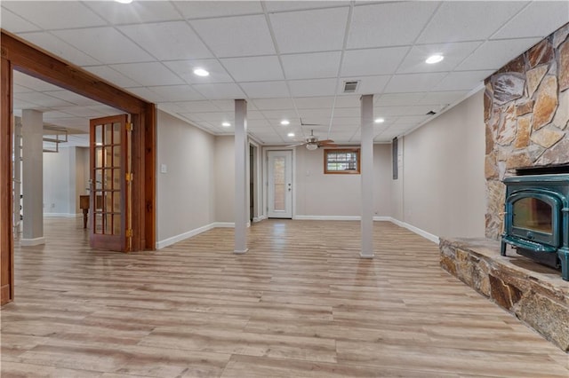 basement with light wood-type flooring, a wood stove, ceiling fan, and a drop ceiling