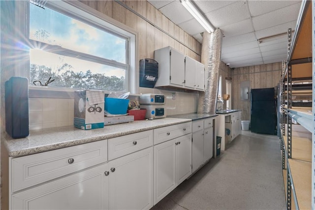 kitchen with electric panel, white cabinetry, black refrigerator, and wood walls